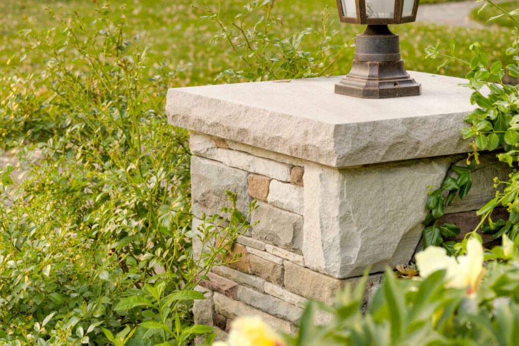 A traditional lantern sits atop a stone pillar surrounded by lush green foliage in a daylight garden setting, exuding a sense of tranquility.