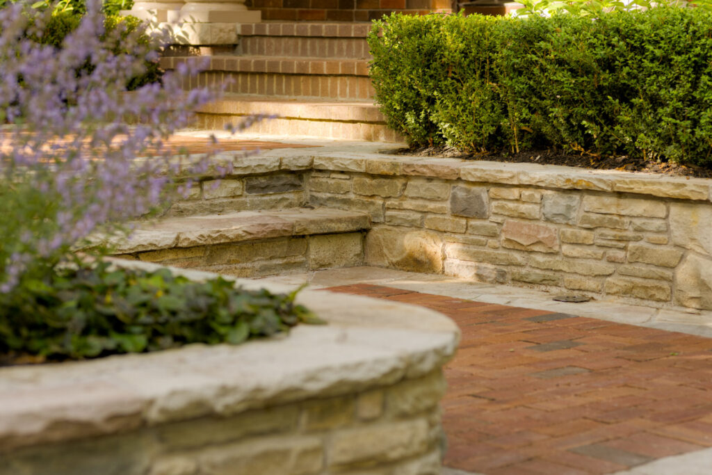 This image features a landscaped garden with stone steps, lush green shrubs, lavender flowers in the foreground, and a brick pathway.